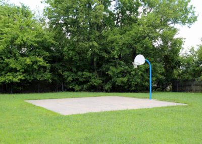 A basketball court situated in a park, surrounded by lush trees and green grass, inviting outdoor sports and recreation