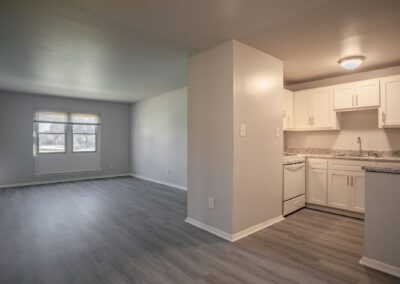 A spacious, empty living room featuring white wall and elegant hardwood floors, showcasing a clean and modern aesthetic.